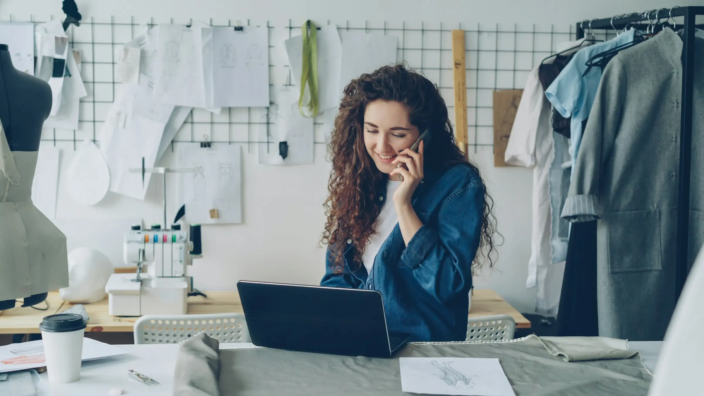 Small business owner on a phone call at her laptop in a clothing studio