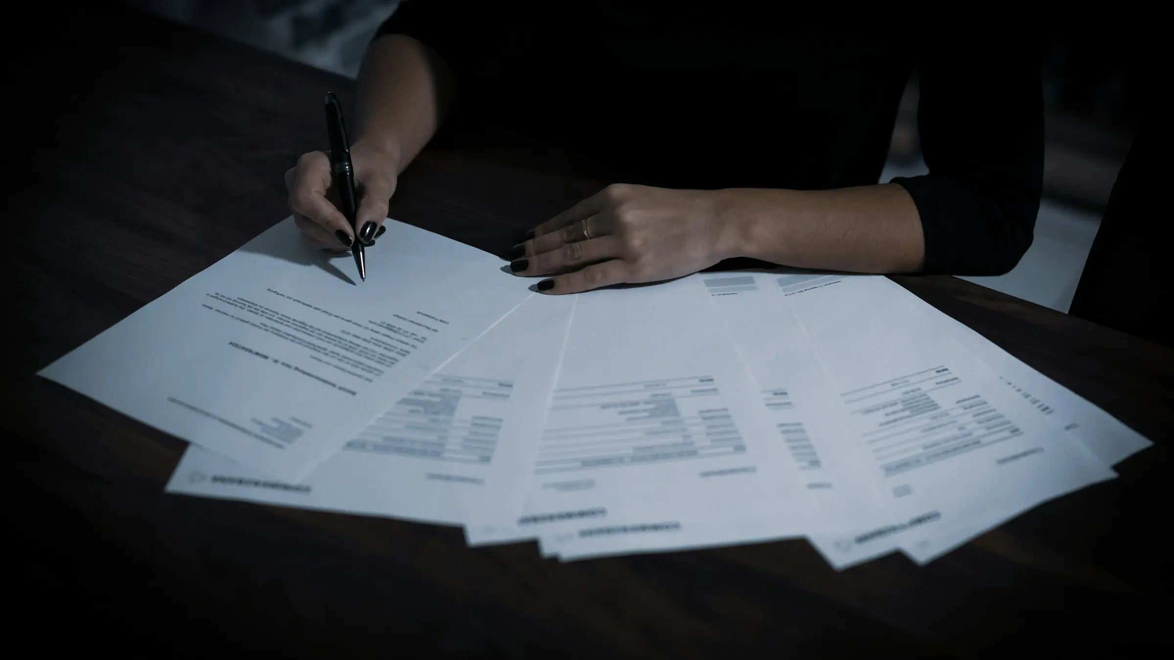 Person signing a contract at a dark desk