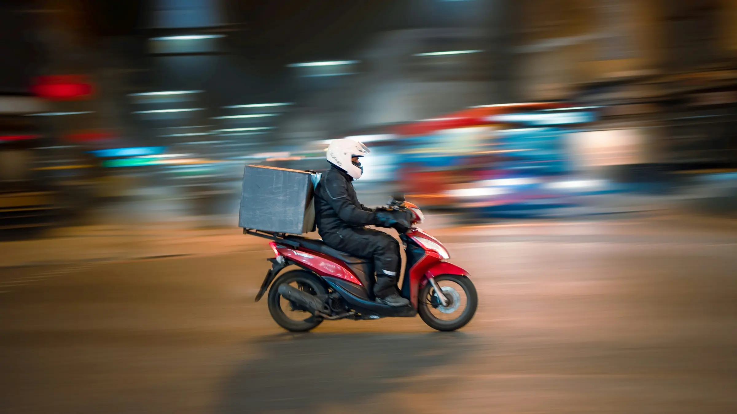 Food delivery courier riding a scooter through the city at night