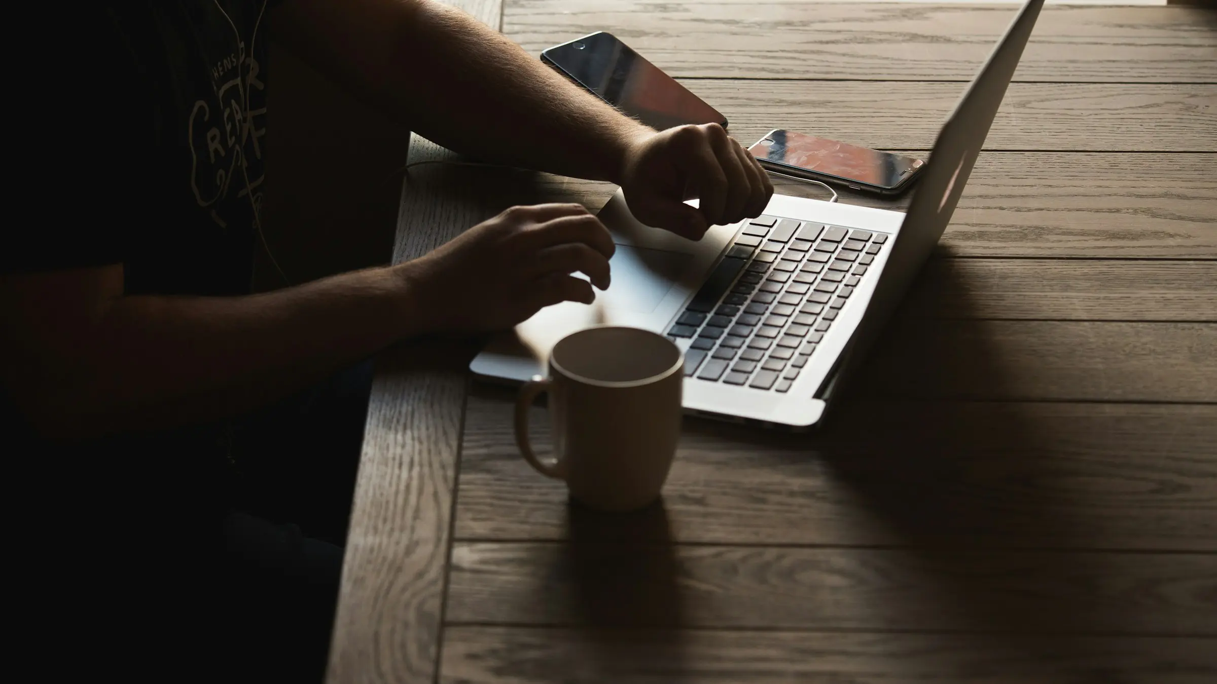 Freelancer typing on a laptop at a wooden cafe table