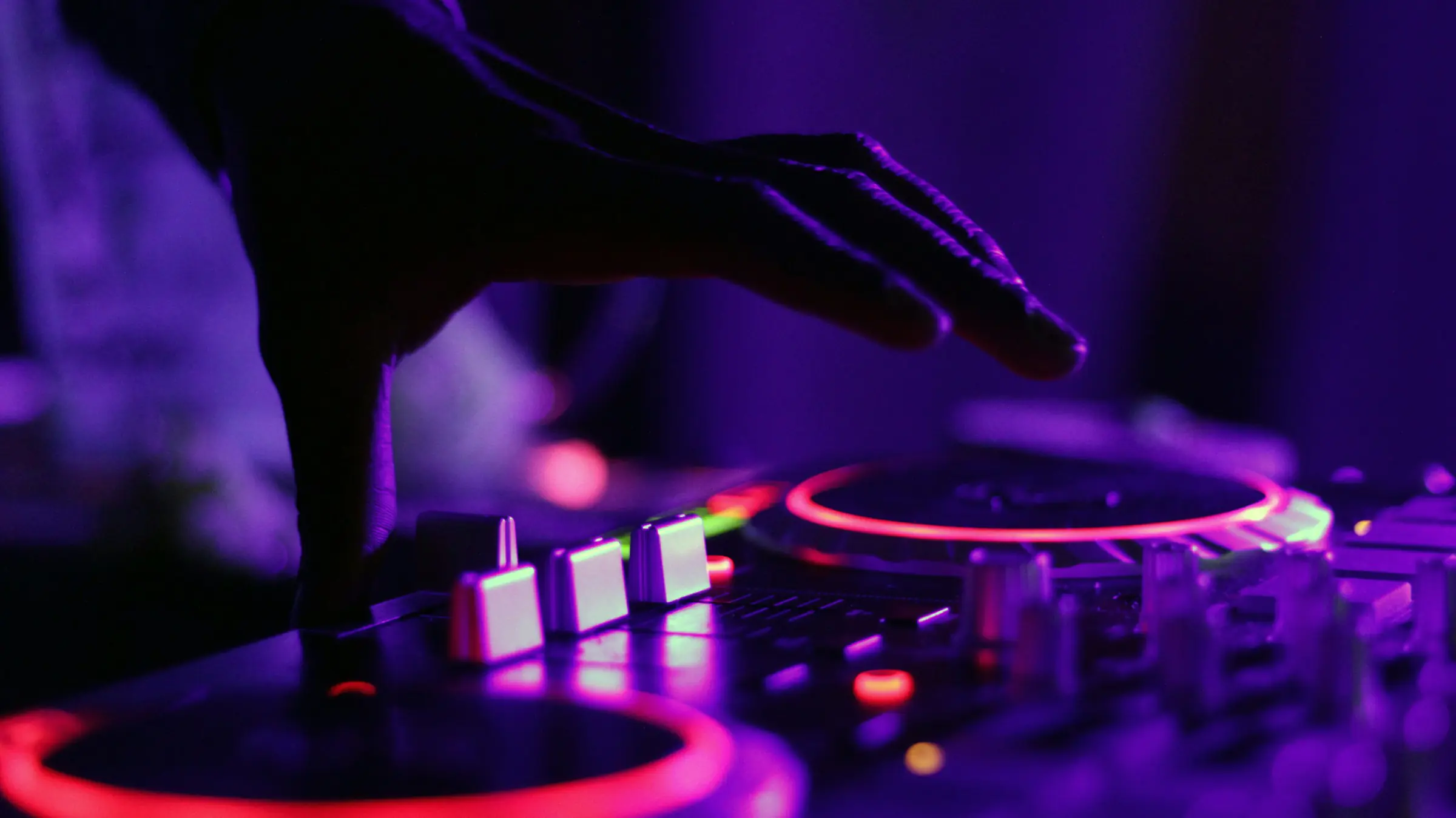 DJ's hand on a mixer under purple club lights