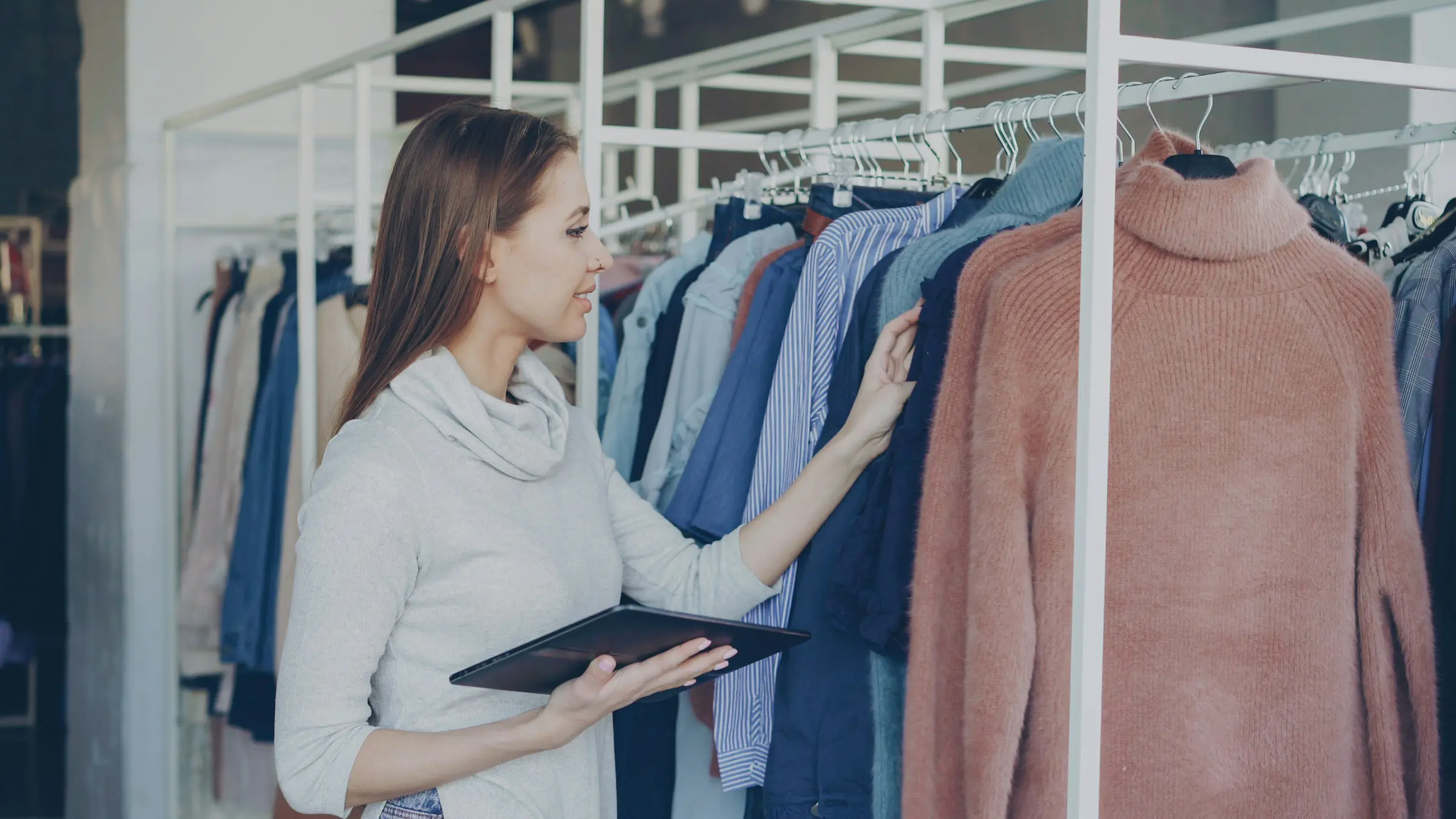 Boutique owner checking a tablet among clothing racks
