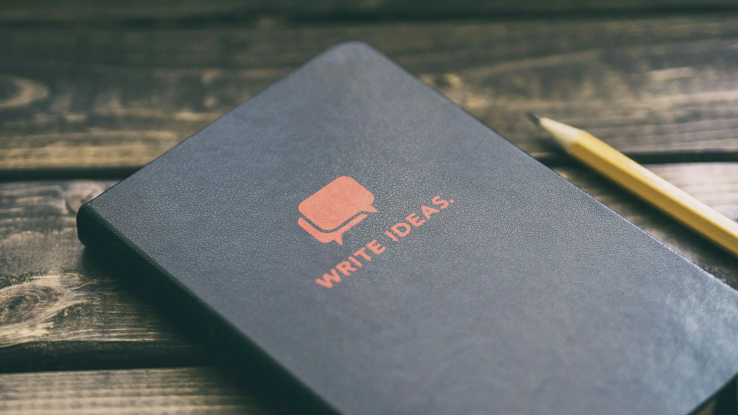 Dark notebook labeled write ideas next to a pencil
