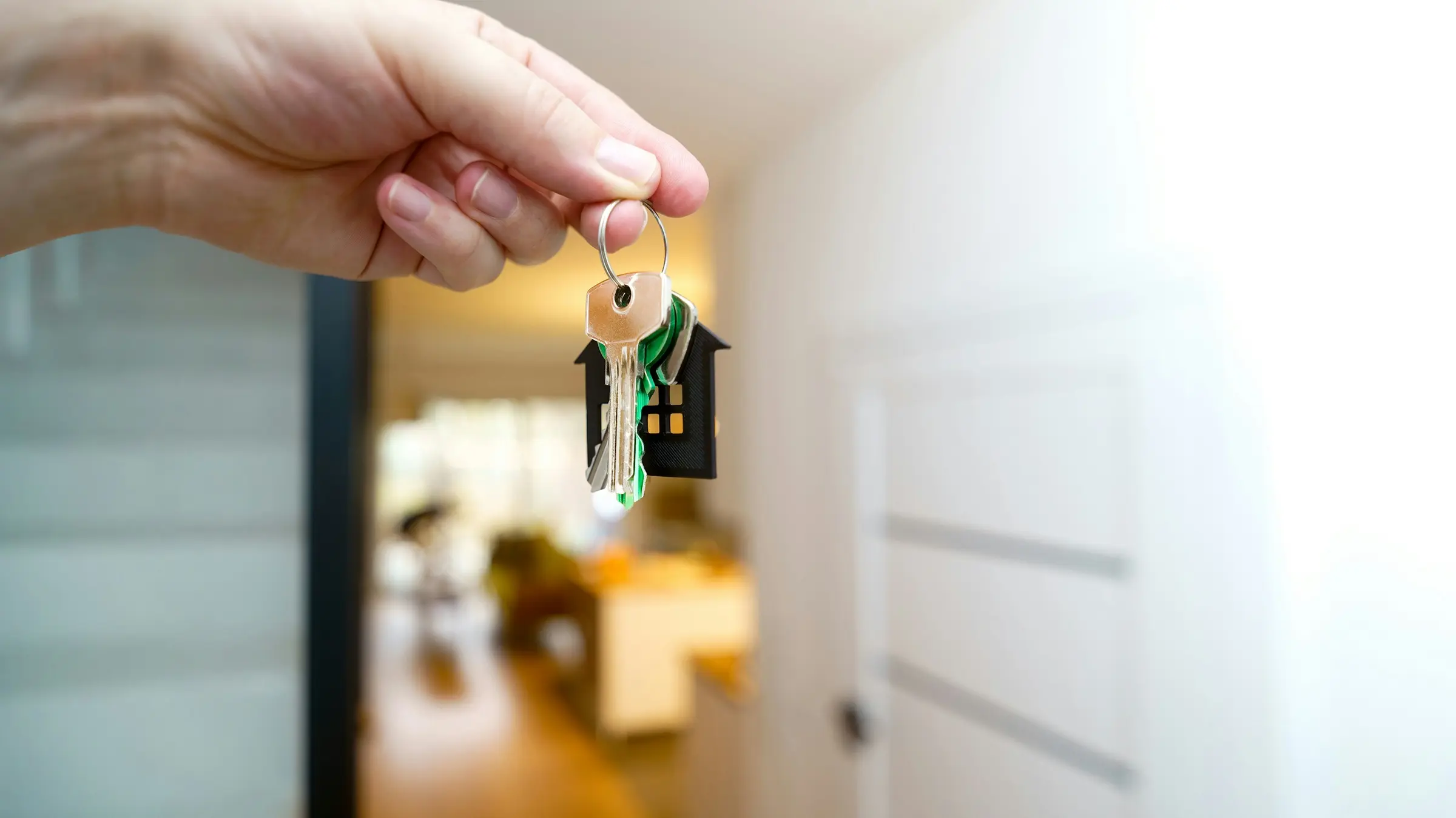 Hand holding house keys with a house keychain in a doorway